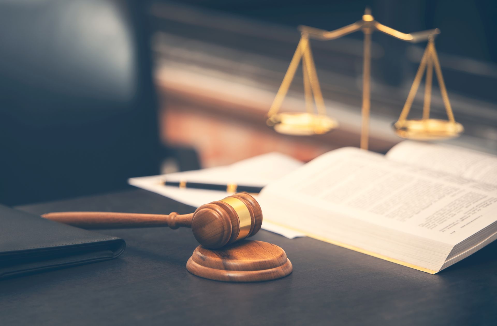 Le marteau d'un juge sur son bureau, à côté d'un livre ouvert et de la balance de la justice, dans un cabinet d'avocats.