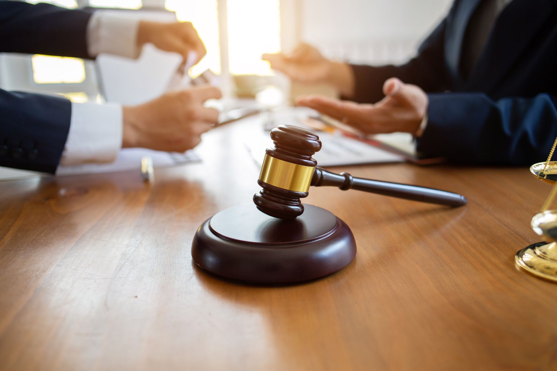 Un marteau d'avocat sur un bureau lors d'une réunion d'affaires, des personnes se serrant la main en arrière-plan.