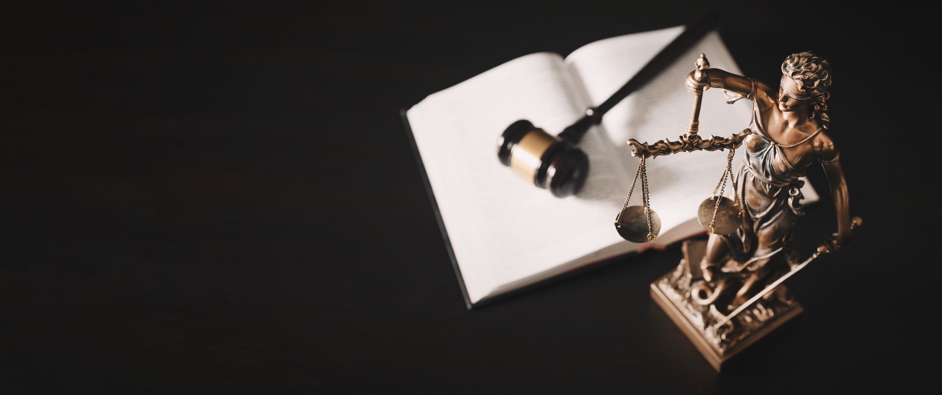 Livre ouvert avec marteau, balance et statuette de la justice en bronze sur fond noir