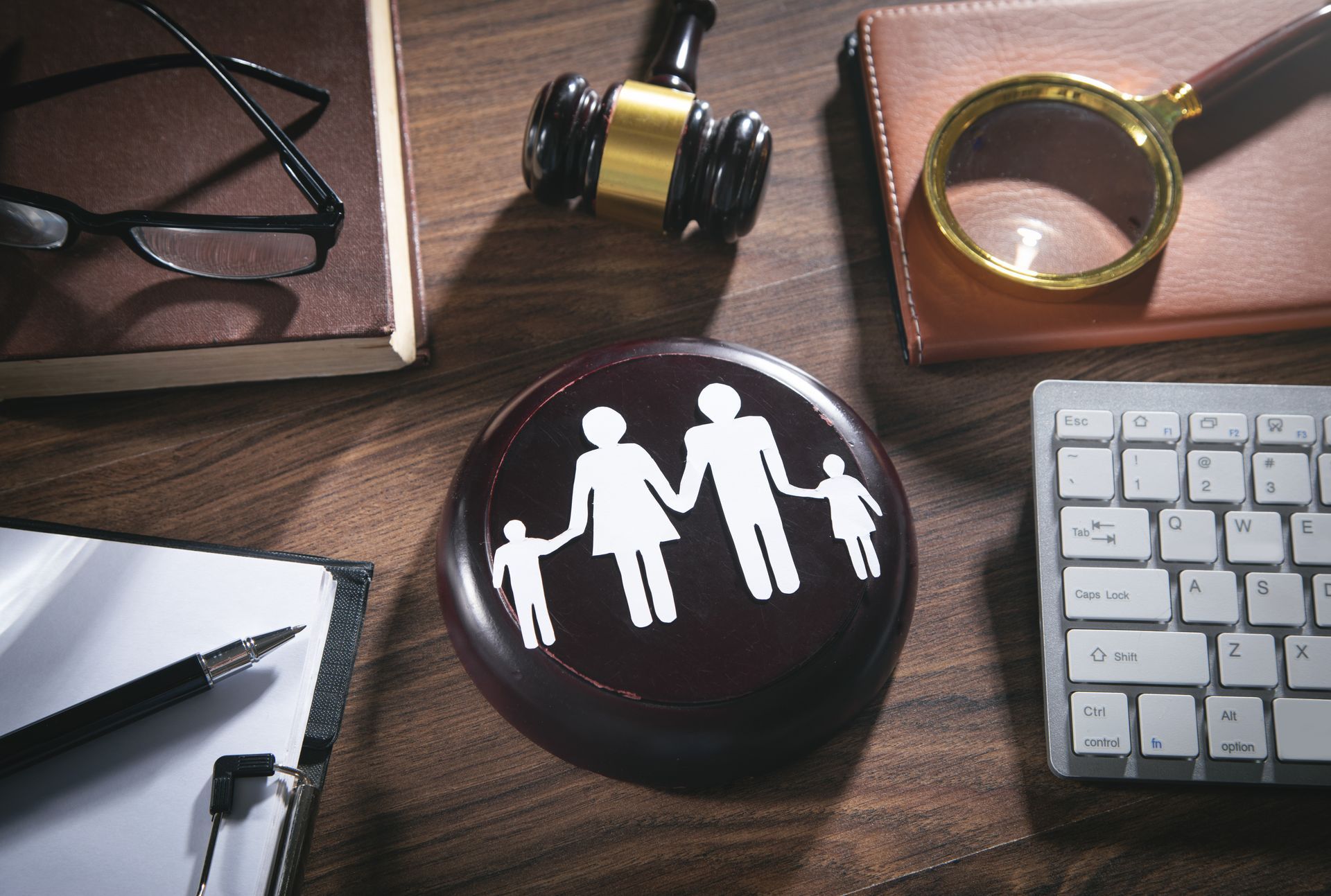 Bureau d'avocat avec bouton représentant une famille, marteau de juge, loupe, clavier et lunettes.