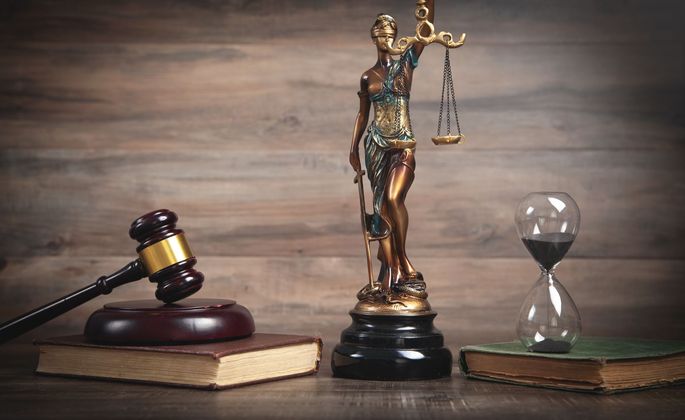 Livre de lois avec maillet, statue de la justice et sablier sur un bureau en bois