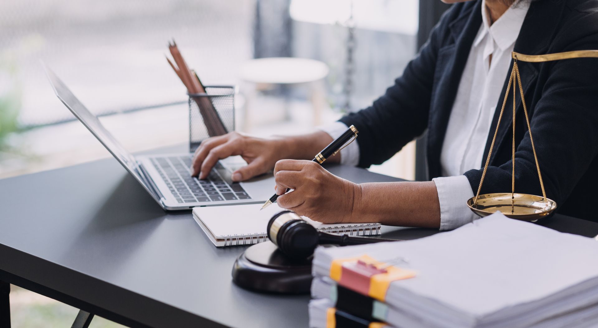 Un avocat, assis à son bureau, utilise son ordinateur portable à côté de la balance de la justice et de piles de documents.