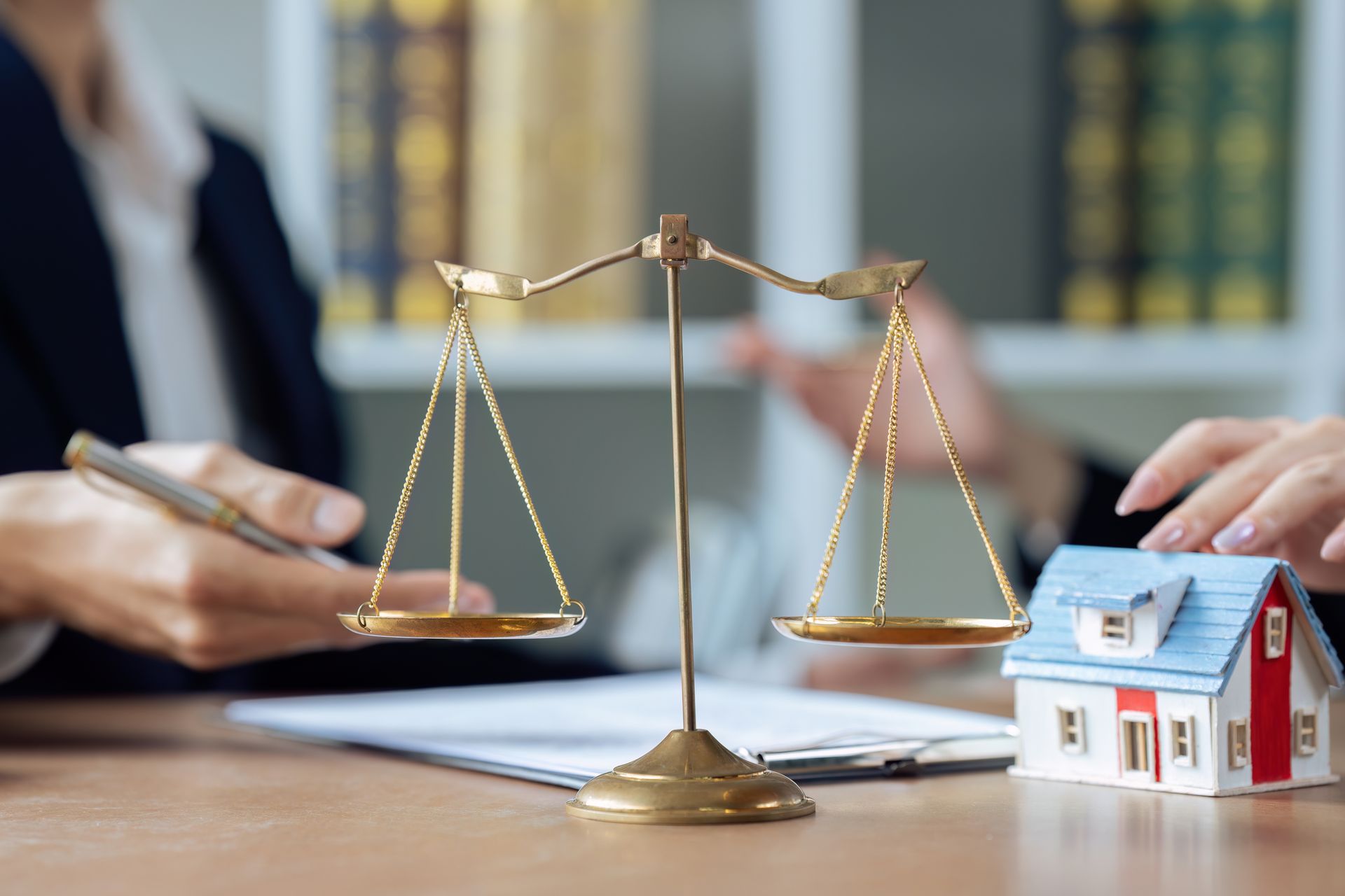 Bureau d'avocat avec balance de la justice et maquette de maison, symbolisant le droit immobilier ou les litiges fonciers.