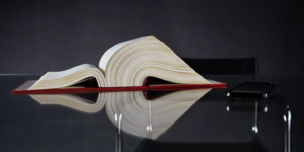 Livre ouvert dont les pages forment un cœur sur une surface noire réfléchissante, avec un trait de crayon rouge sur la couverture