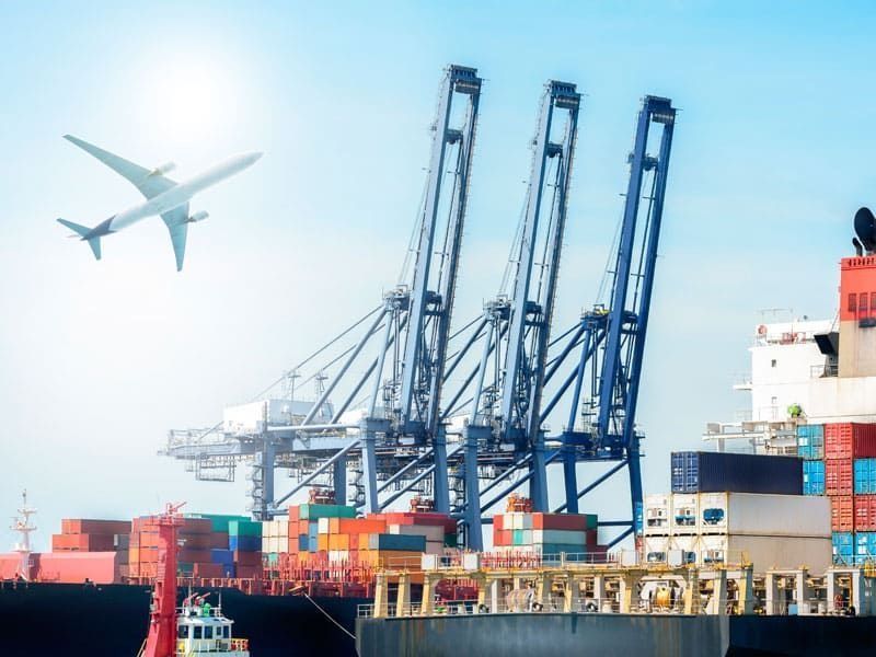 Un avión está volando sobre un barco de carga en un puerto.