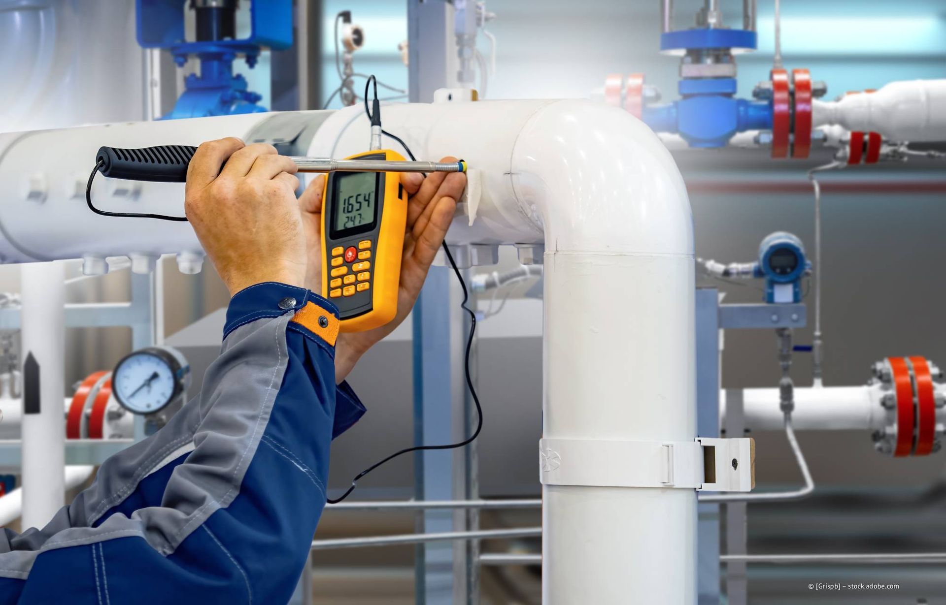 Eine Person benutzt ein gelbes Gerät, um die Temperatur eines weißen Rohres zu messen.