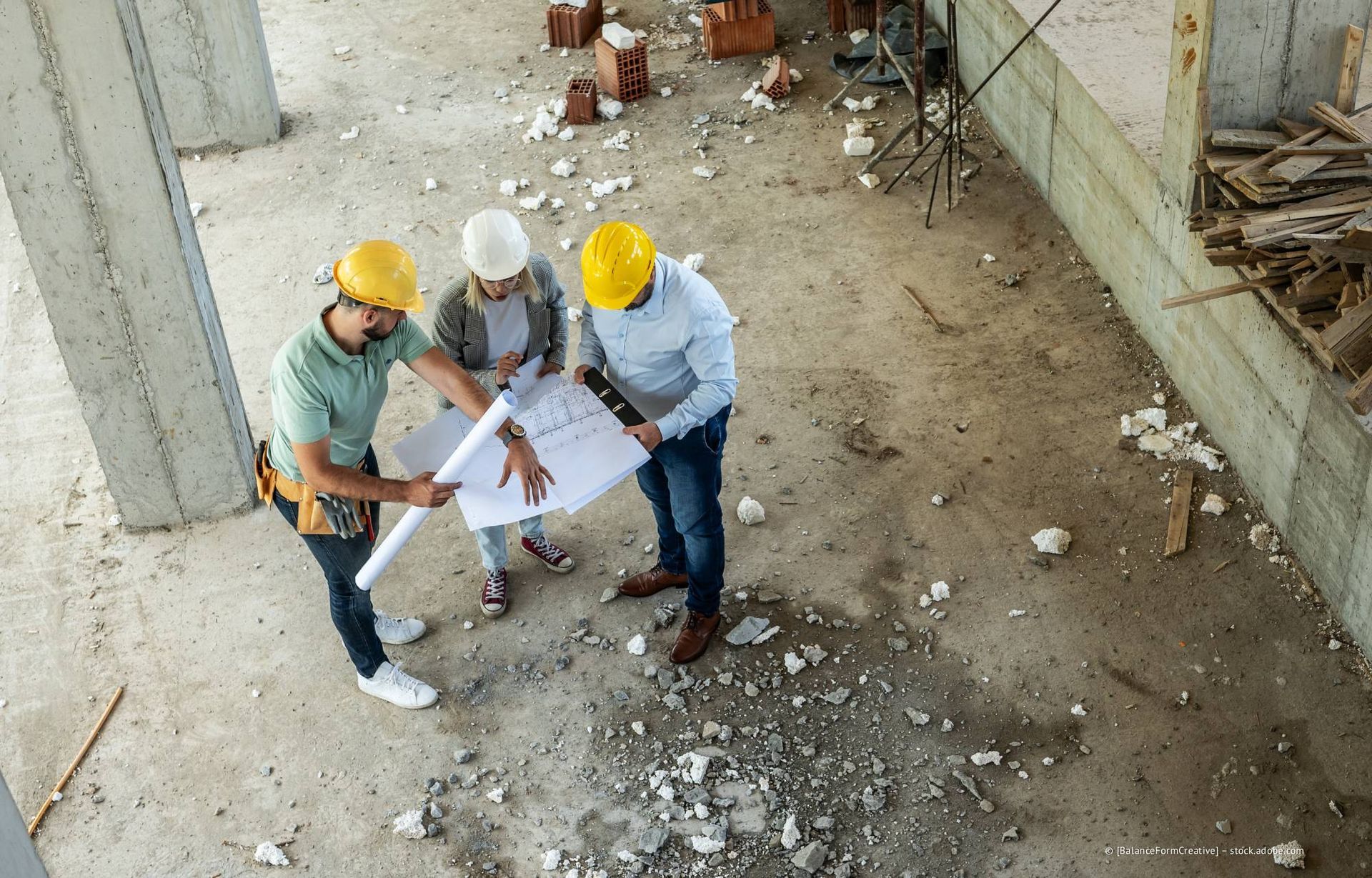 Bauarbeiter mit Schutzhelmen prüfen Baupläne auf einer Baustelle.