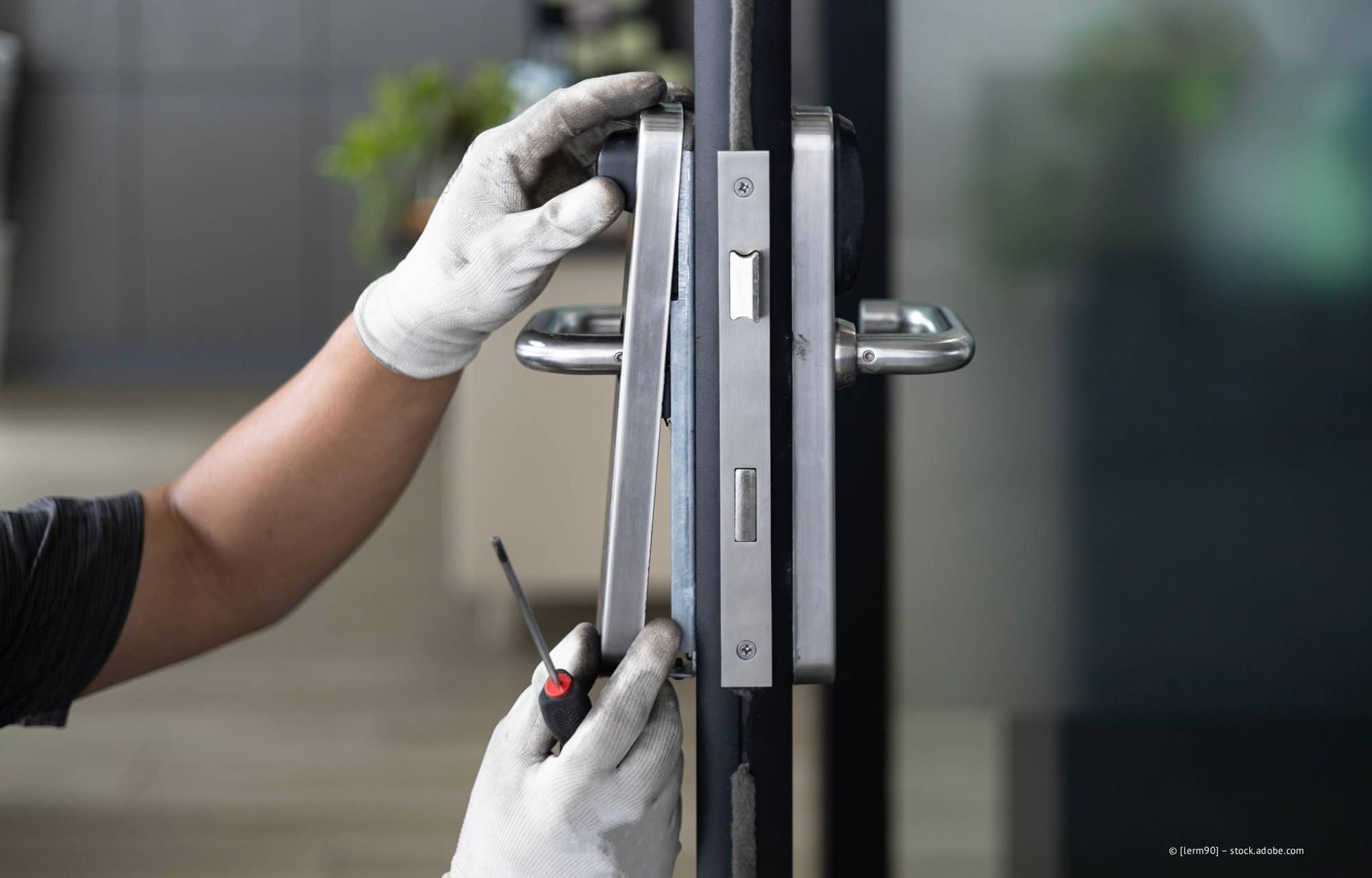 Eine Person mit Handschuhen montiert mit einem Schraubenzieher einen Türgriff an einer Glastür.