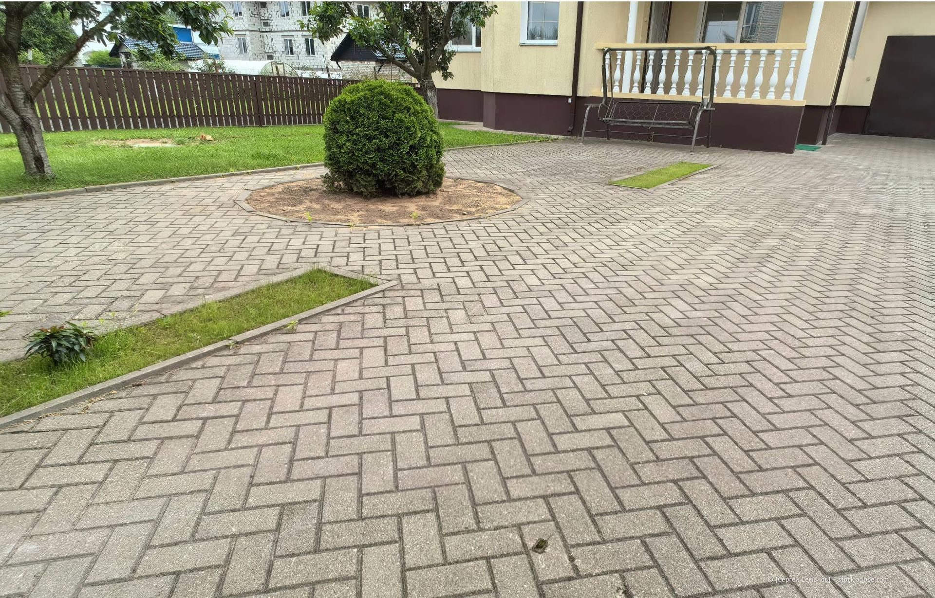 Eine mit Ziegelsteinen gepflasterte Auffahrt mit kleinen Grasstreifen, ein Haus und eine Hecke in der Mitte.