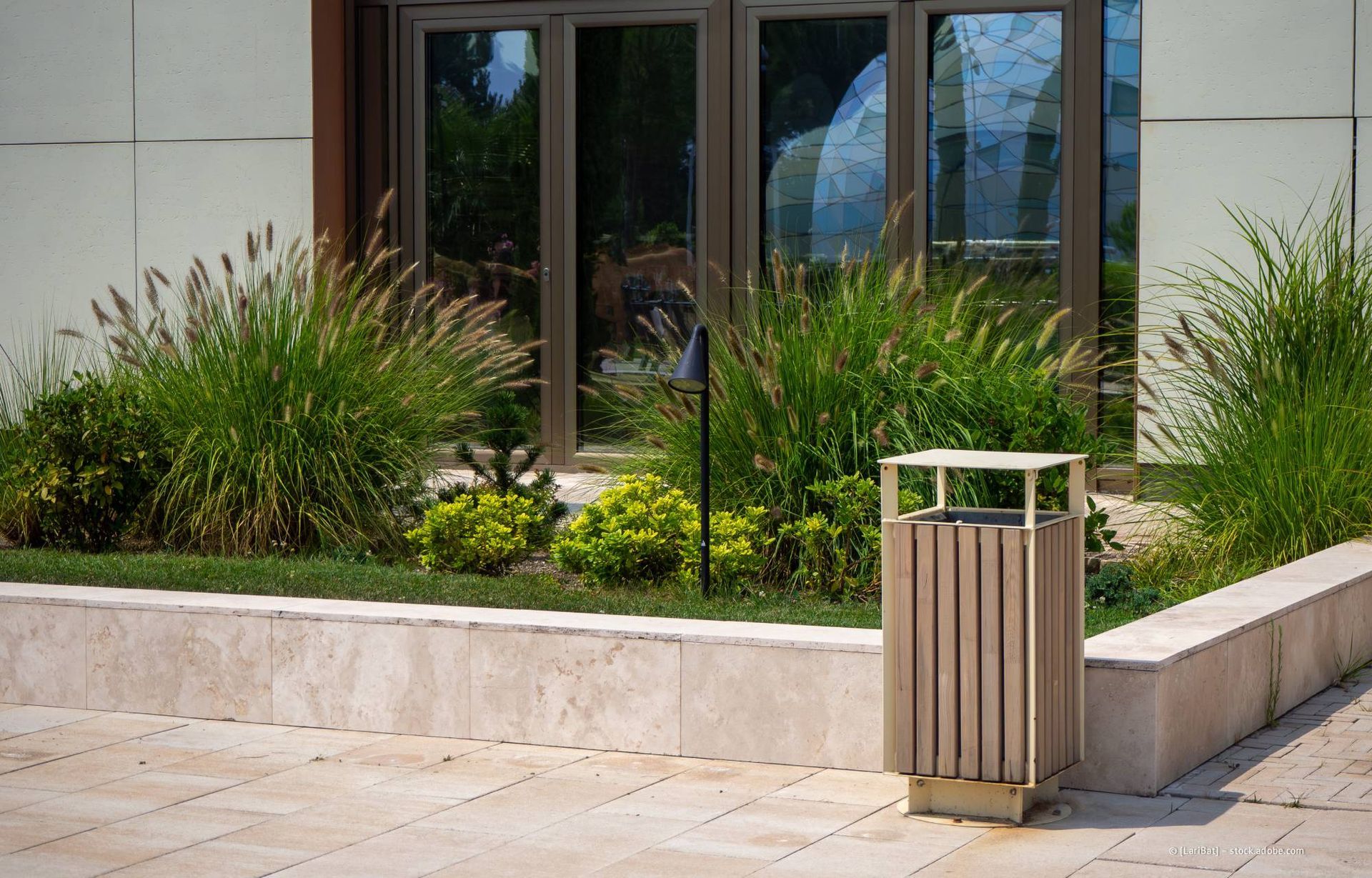 Ein Mülleimer auf einer Steinterrasse, im Hintergrund Grünanlagen und ein Gebäude.