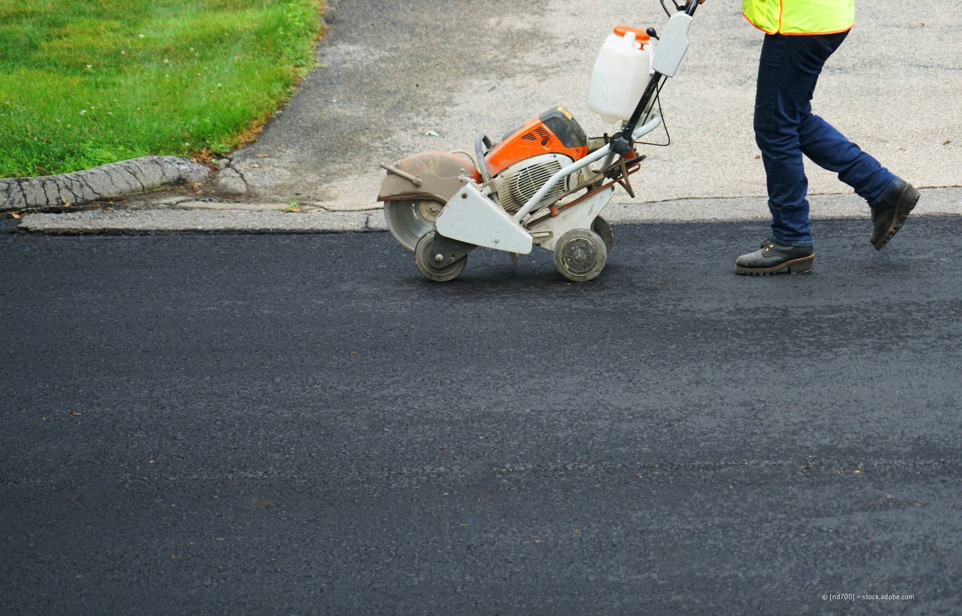 Eine Person schiebt eine Betonsäge, um Asphaltbeläge zu schneiden.