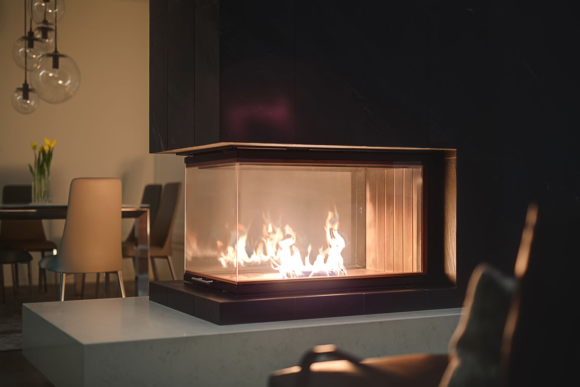 Salon moderne avec une cheminée vitrée aux flammes éclatantes jouxtant un coin repas.
