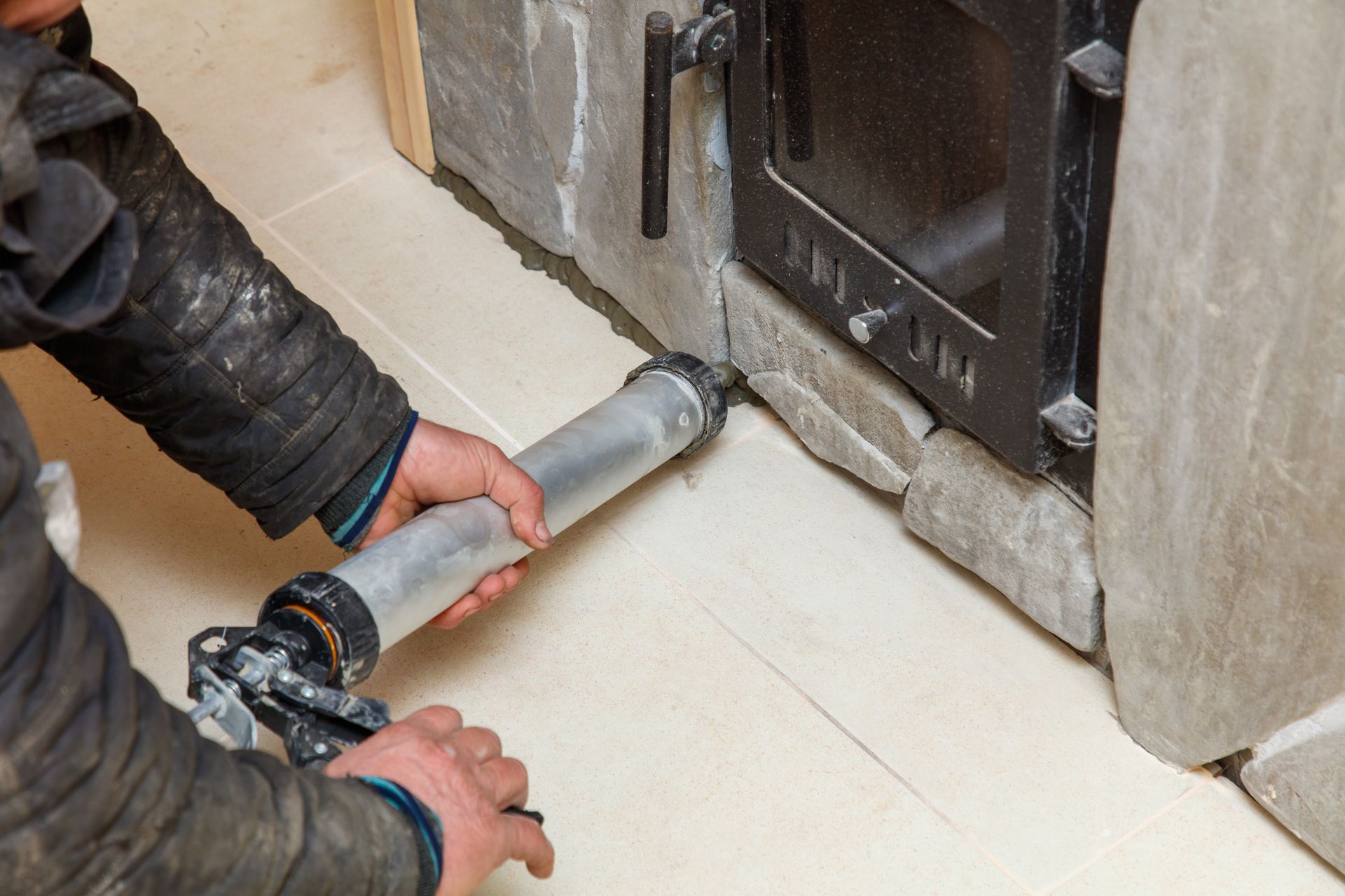 Un ouvrier applique du mastic autour de la base d'une cheminée à l'aide d'un pistolet à calfeutrer.