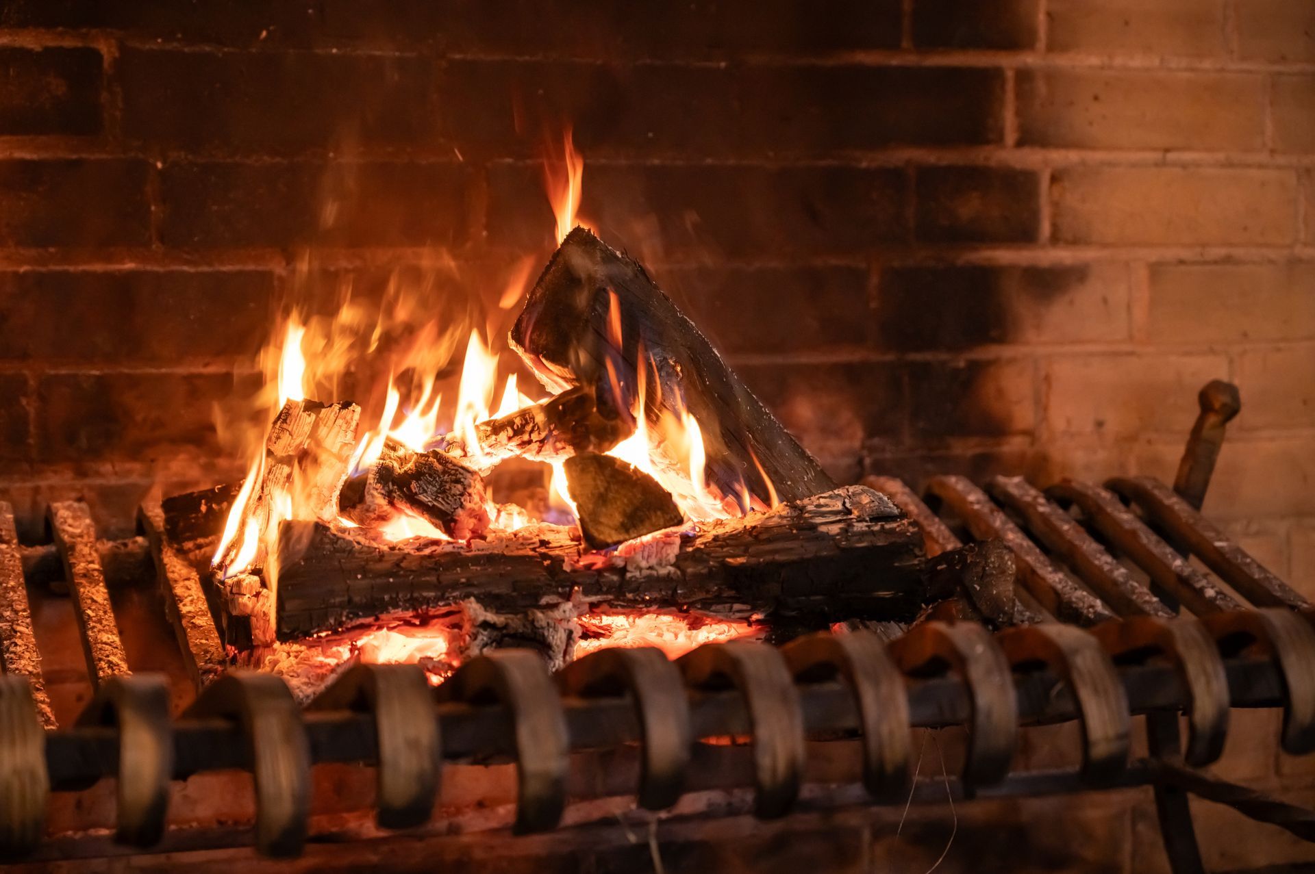 Un feu brûle dans une cheminée en briques, avec des bûches sur une grille métallique.