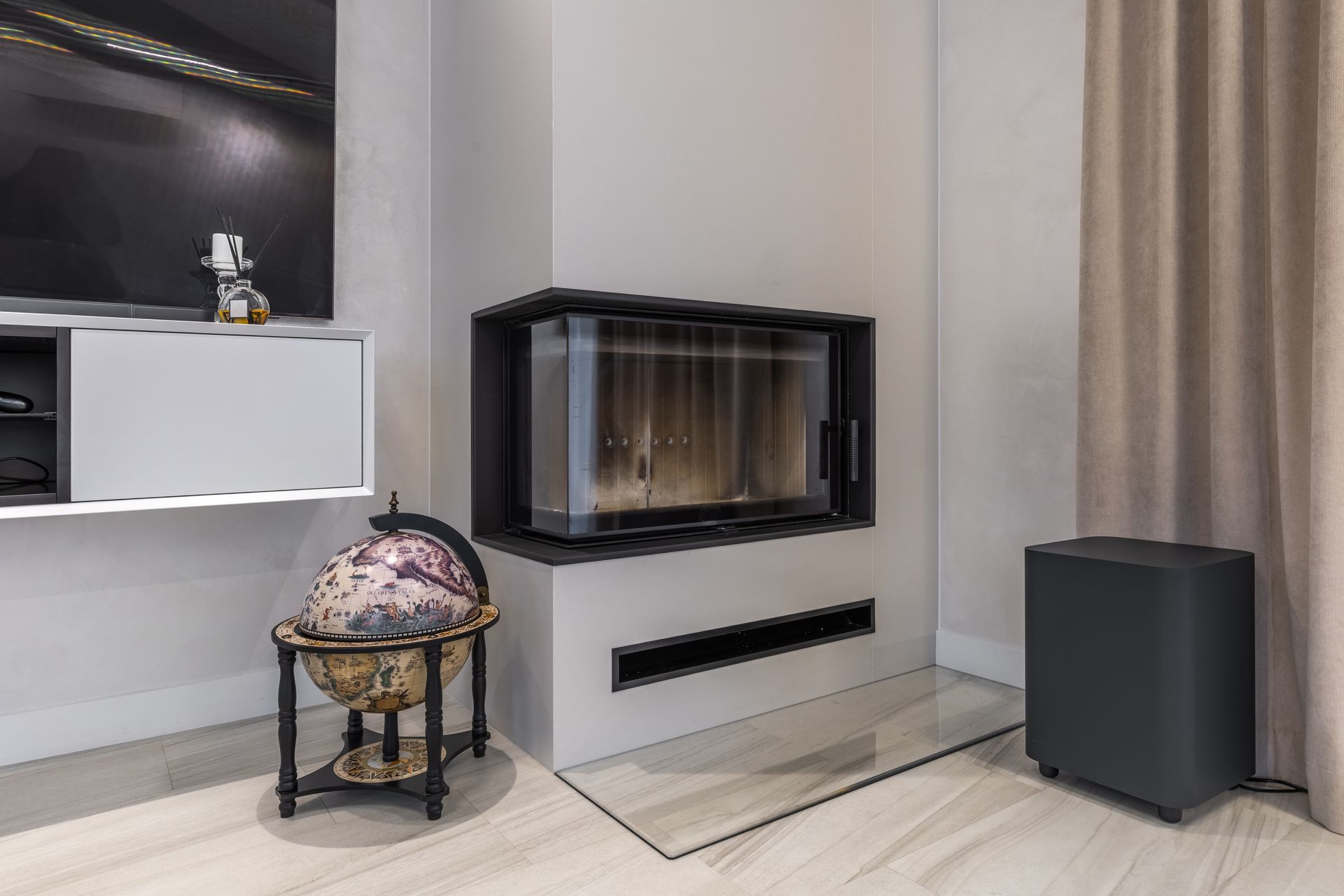 Salon moderne avec cheminée murale, radiateur noir, globe décoratif et rideaux.