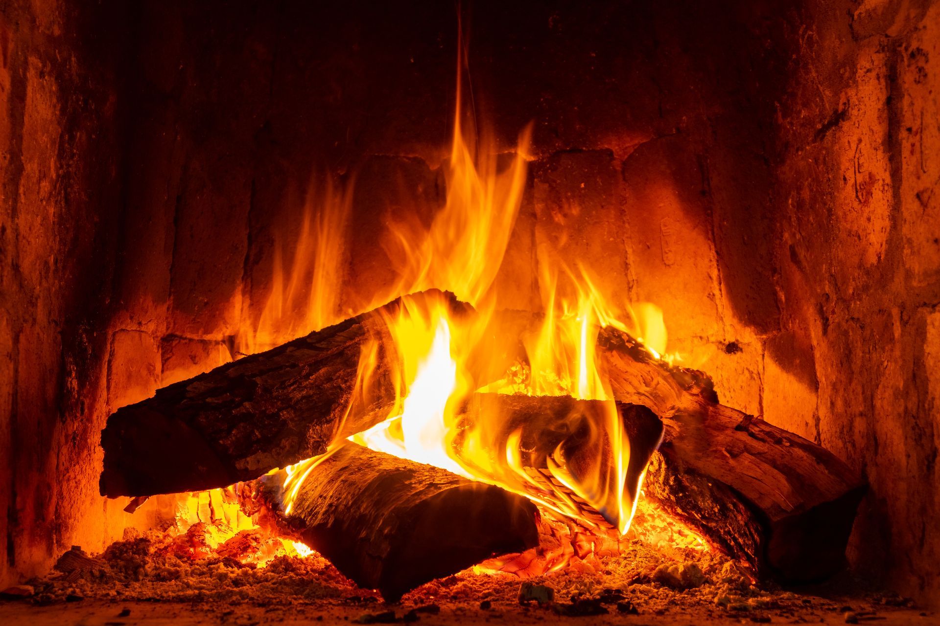 Des flammes et des braises d'un orange vif brûlent dans une cheminée en briques.
