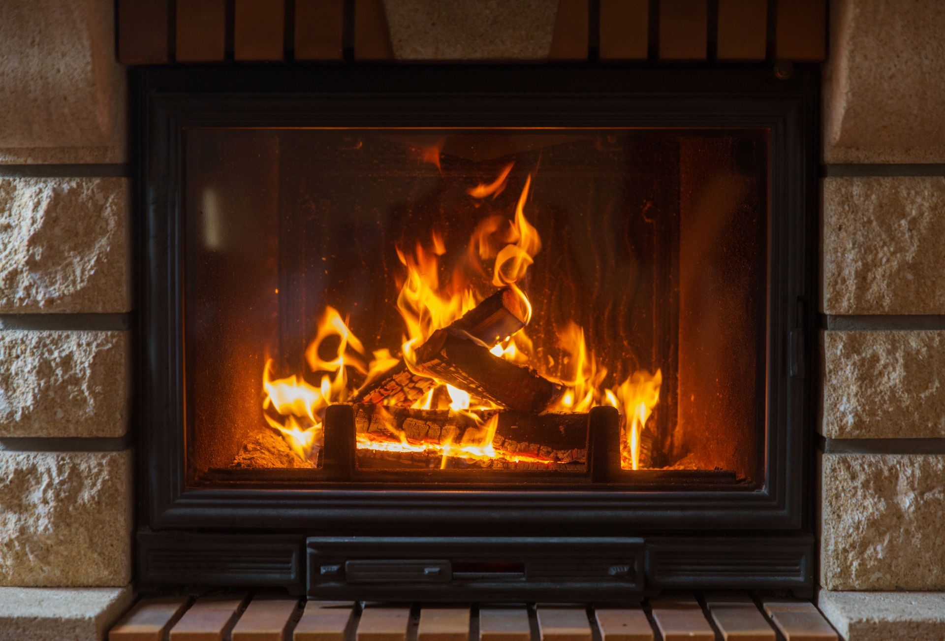 Cheminée allumée avec des flammes vives et des bûches incandescentes dans un foyer en briques.