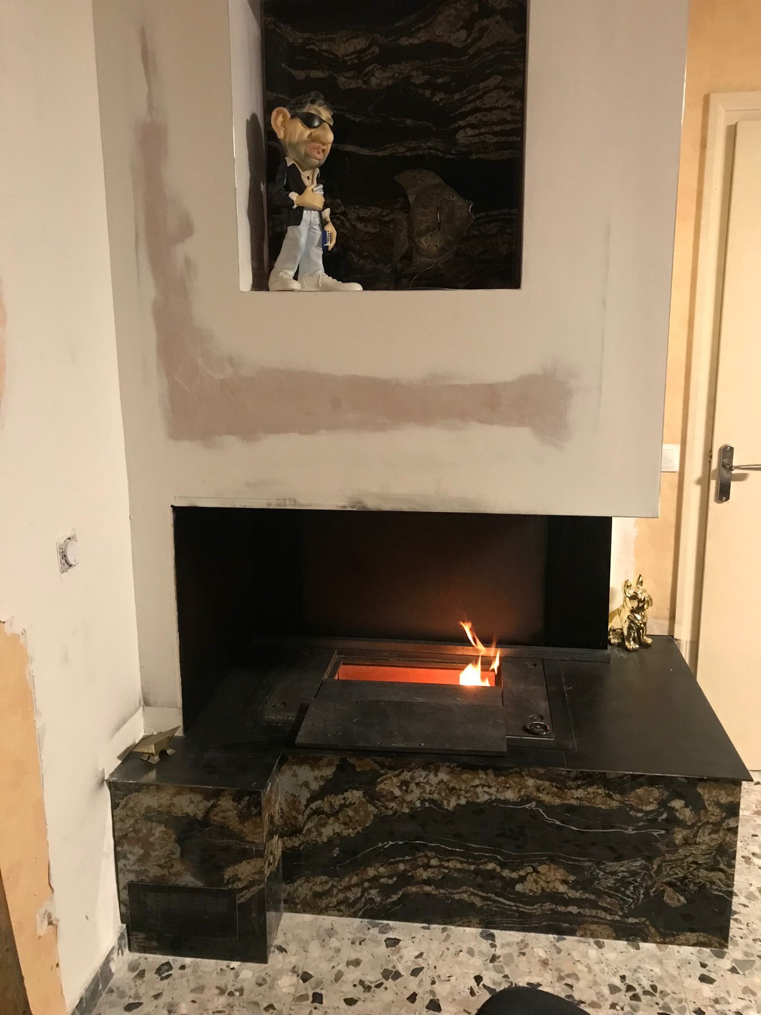 Cheminée du salon avec une petite flamme et une figurine décorative dans la niche murale au-dessus.