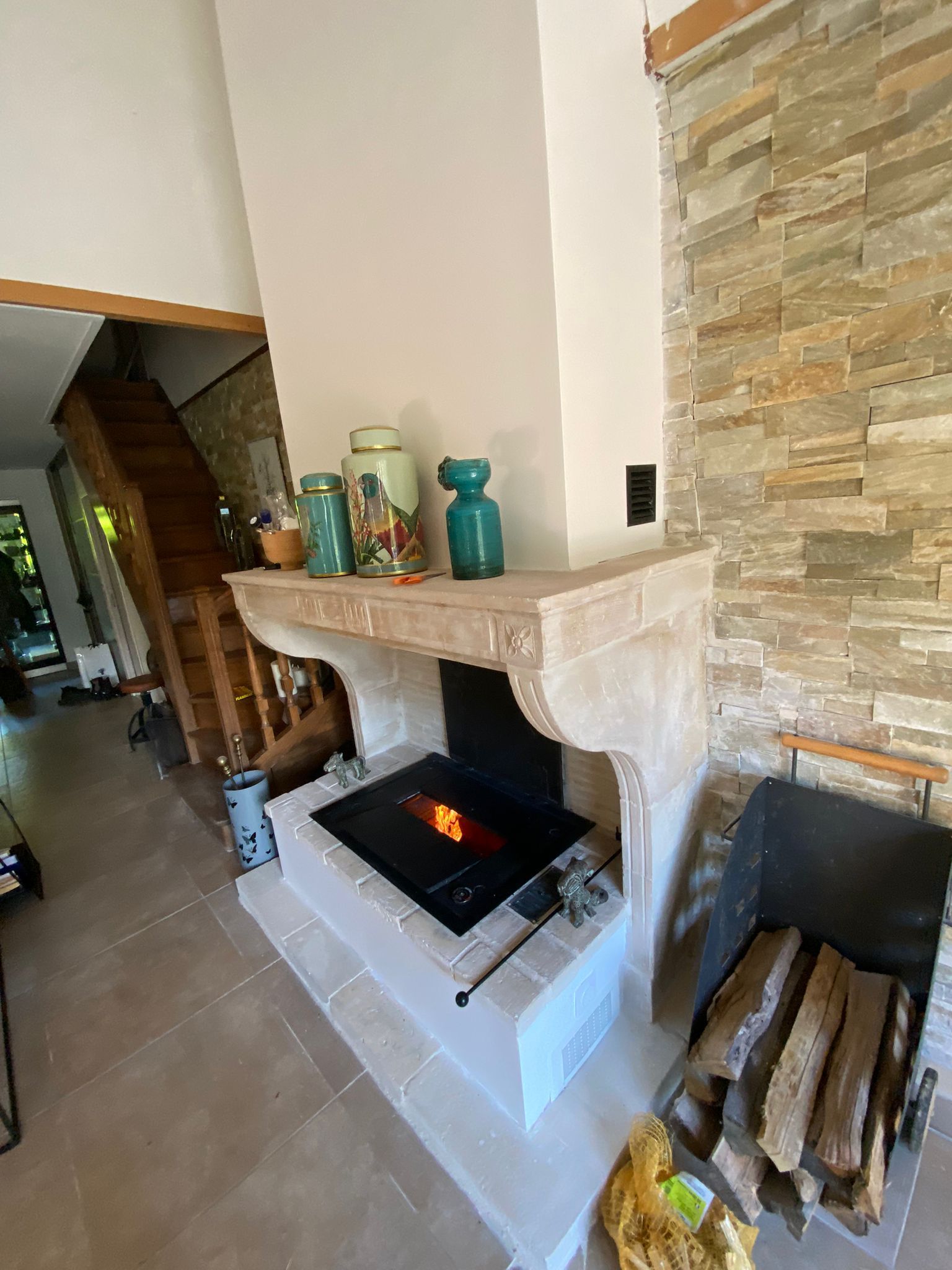 Cheminée du salon avec entourage en pierre, décoration de la cheminée et bois de chauffage empilé à côté d'un poêle à bois noir.