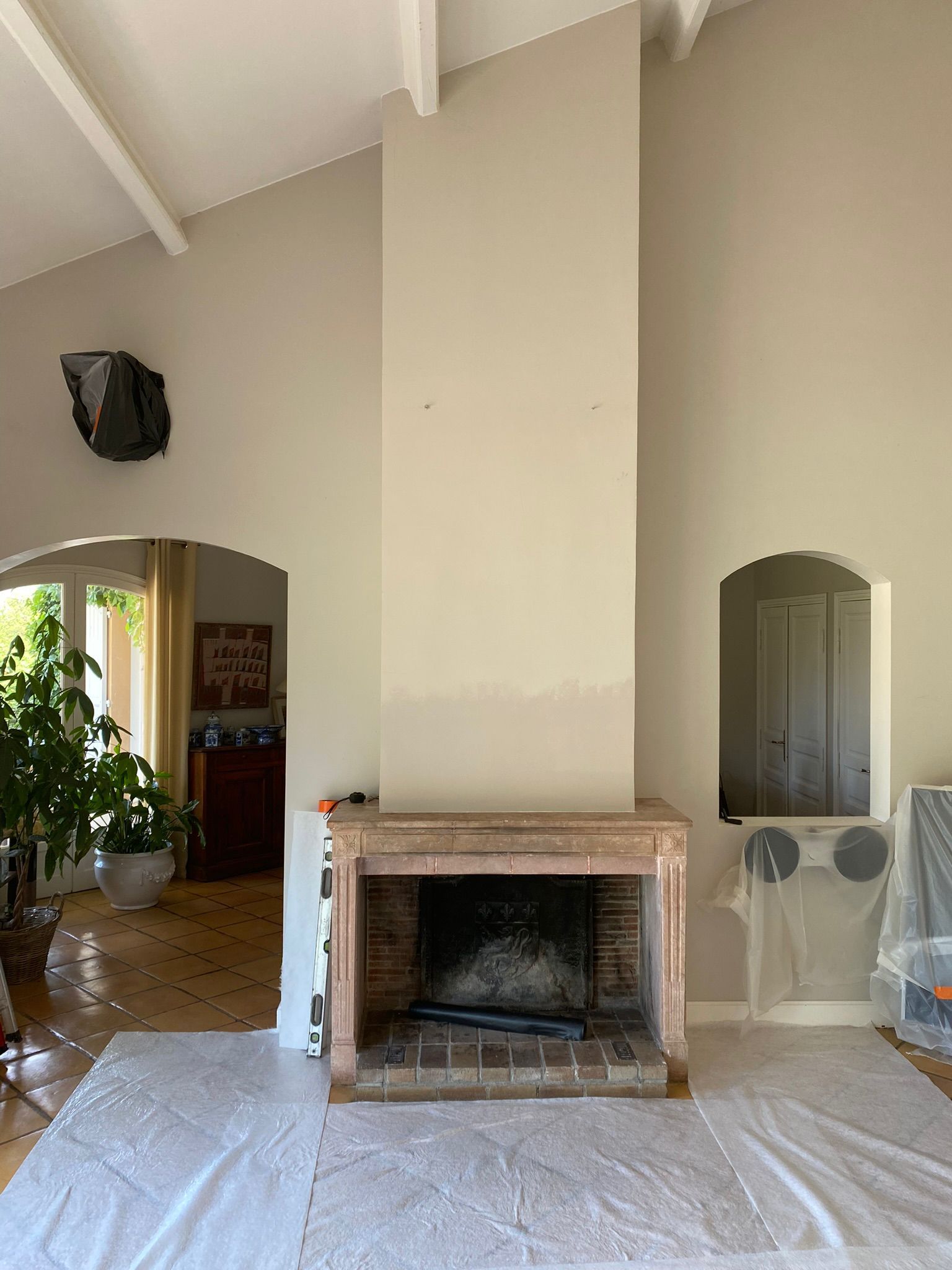 Salon avec cheminée en pierre, haut plafond blanc et portes cintrées, partiellement recouvert pour rénovation.