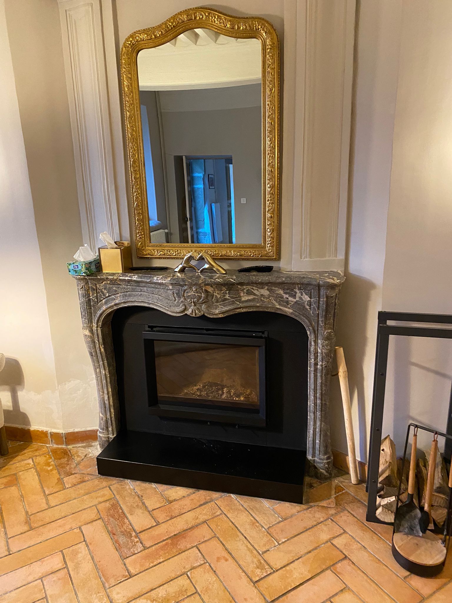 Miroir doré sculpté et orné au-dessus d'une cheminée noire avec manteau en pierre et parquet.