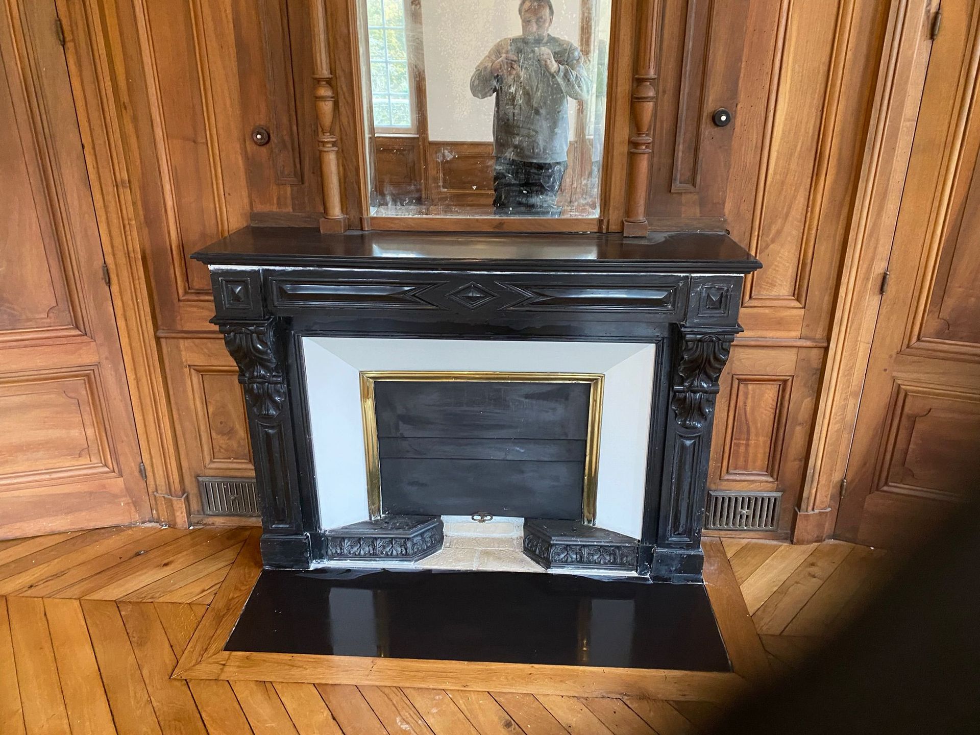 Cheminée en marbre noir avec miroir dans une pièce lambrissée avec parquet.
