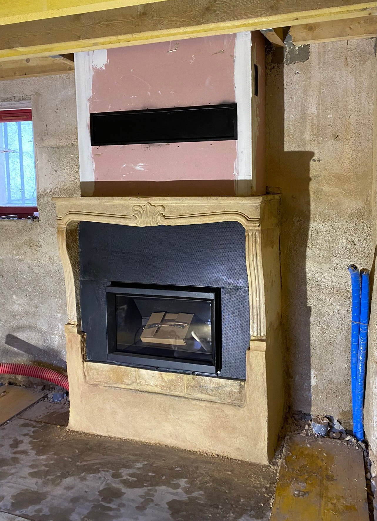 Cheminée partiellement finie avec insert noir et panneau supérieur rose dans un mur intérieur brut.