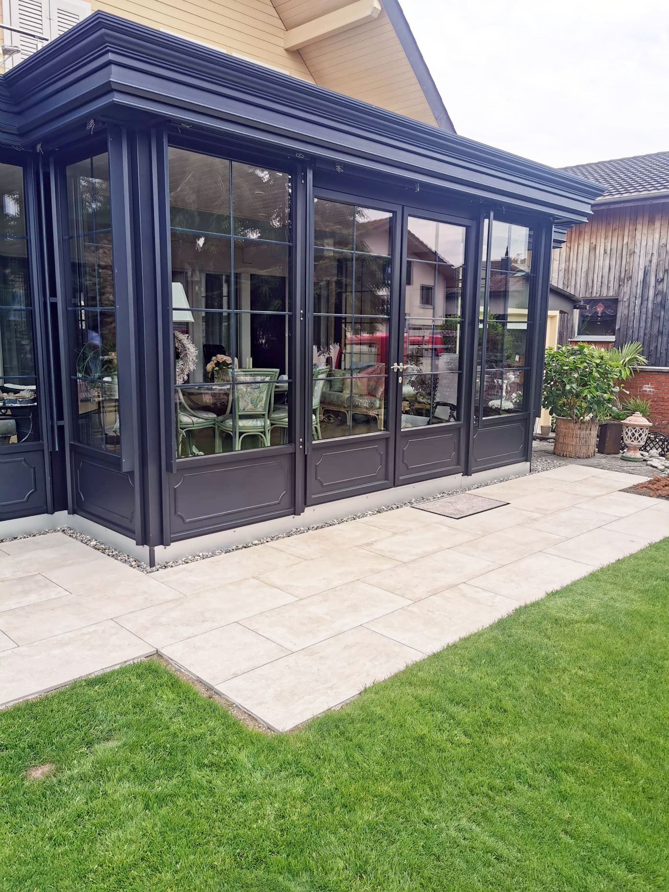 Ein großer Wintergarten mit vielen Fenstern und einer Terrasse vor einem Haus.