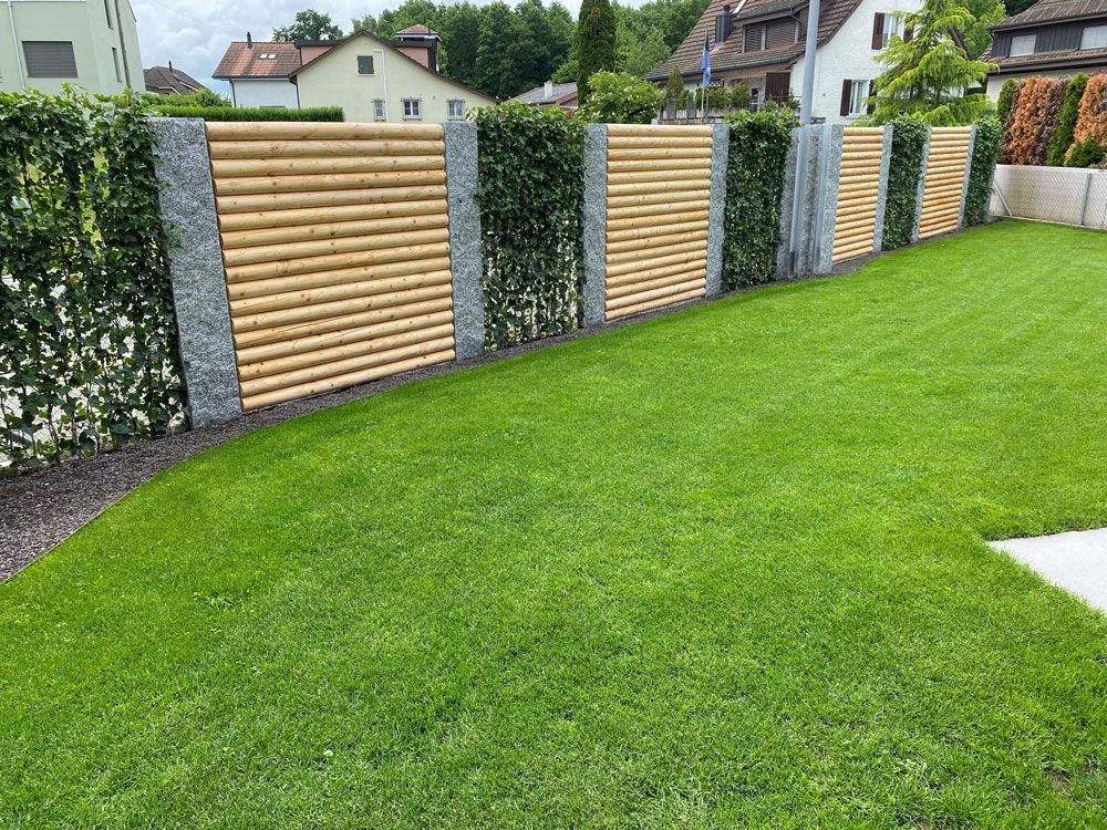 Ein Gärtner kniet, hält eine Gartengabel und lächelt. Blumen und Sträucher im Garten.