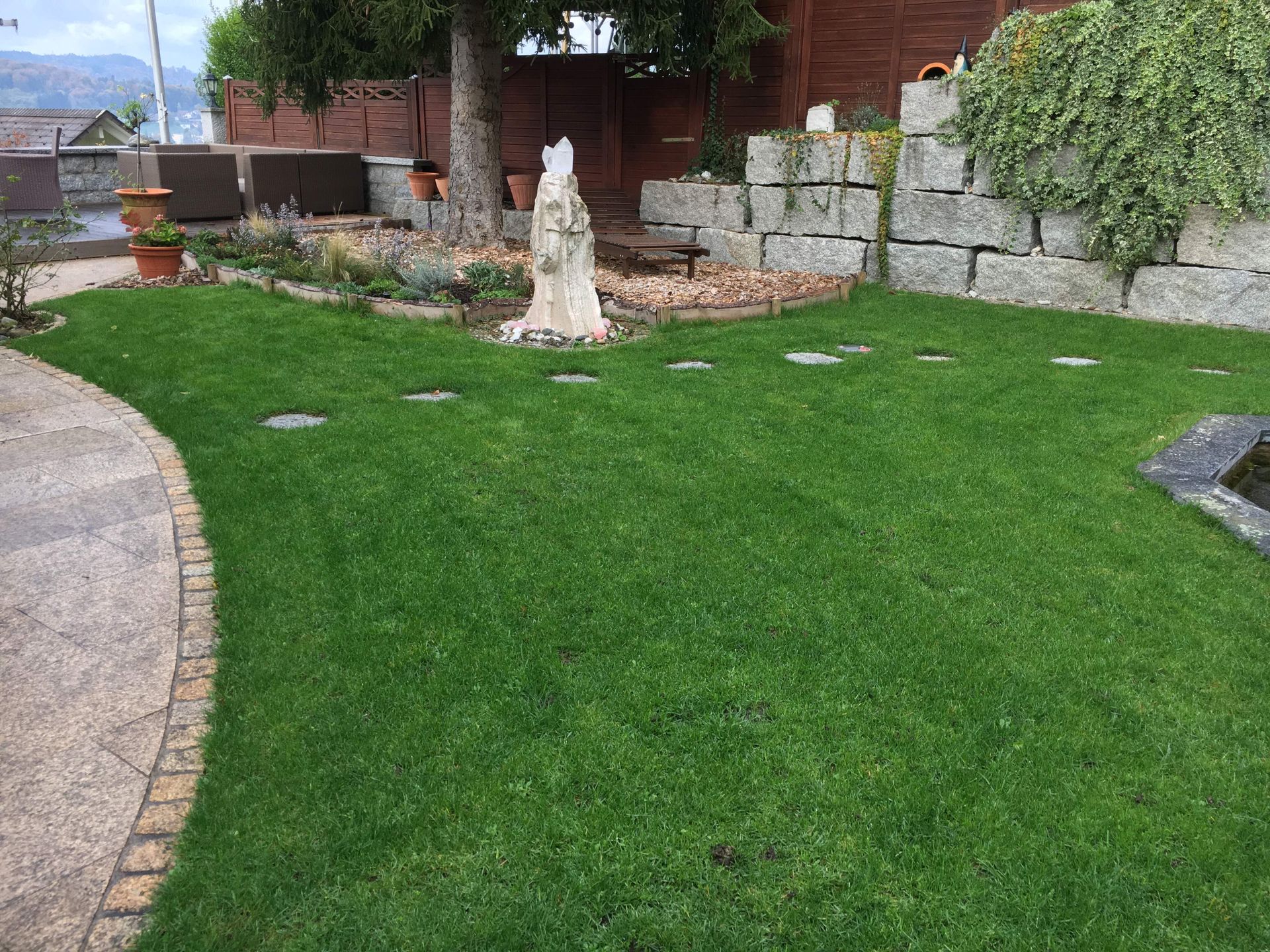 Ein üppiger grüner Rasen mit einer Steinmauer und einem Brunnen in der Mitte.
