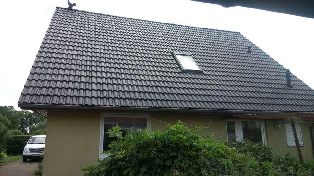 Ein Haus mit einem schwarzen Ziegeldach und einem davor geparkten weißen Lieferwagen.