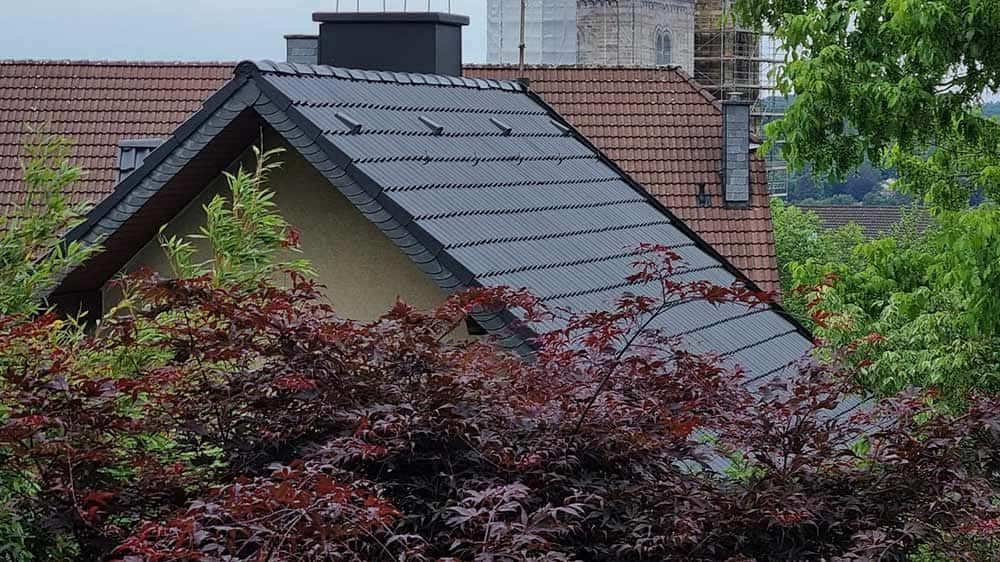 Ein Dach eines Hauses mit einem Schornstein und Bäumen im Vordergrund