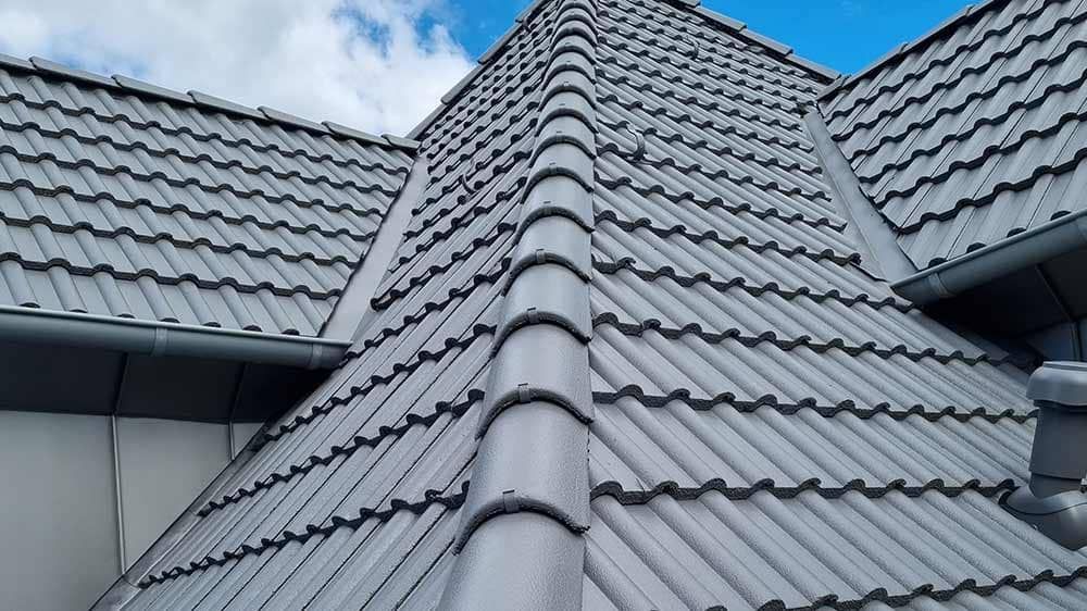 Eine Nahaufnahme eines grauen Ziegeldachs mit einem blauen Himmel im Hintergrund.