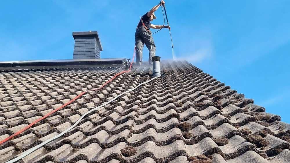 Ein Mann reinigt das Dach eines Hauses mit einem Hochdruckreiniger.