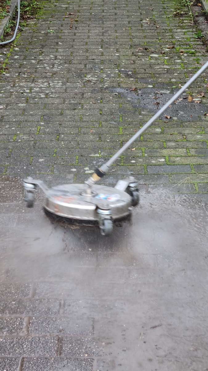 Eine Person verwendet einen Hochdruckreiniger, um einen Ziegelweg zu reinigen.