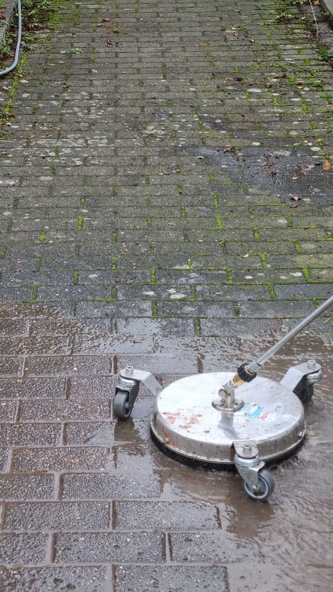 Eine Person reinigt einen Ziegelweg mit einer Maschine.