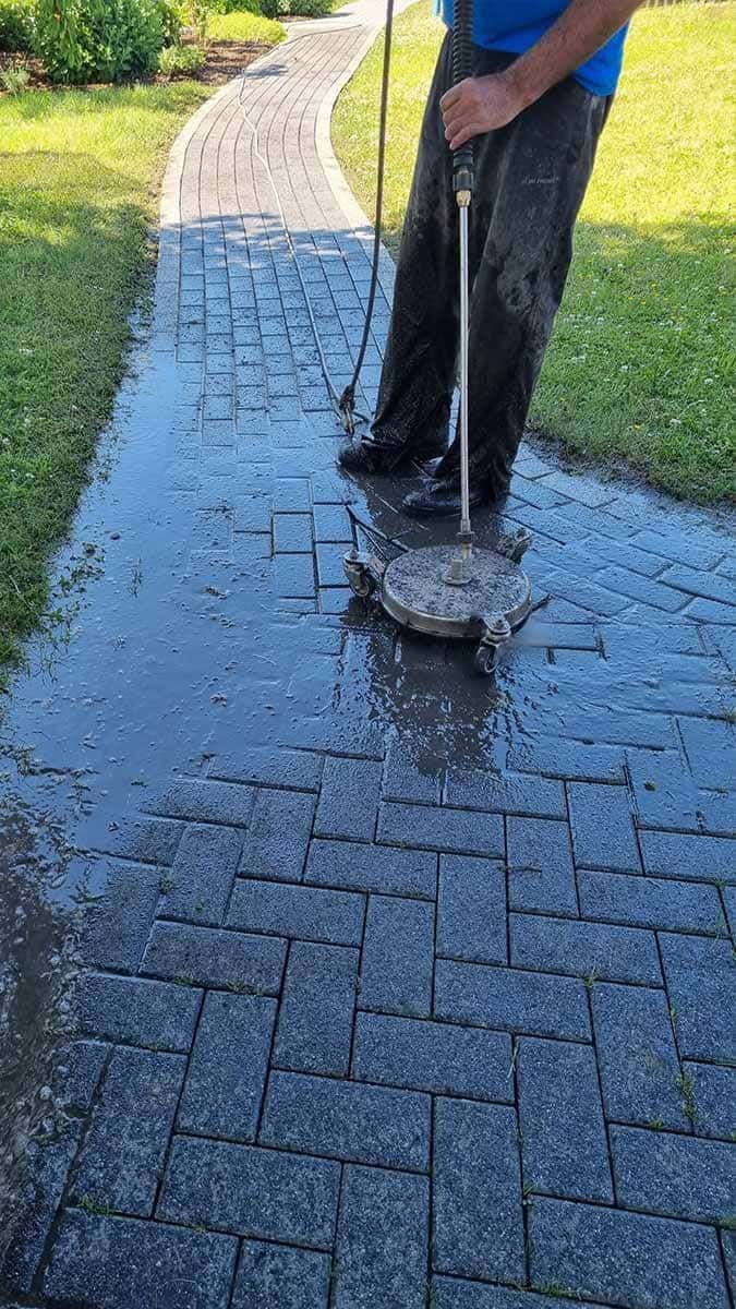 Ein Mann reinigt einen Ziegelweg mit einem Hochdruckreiniger.