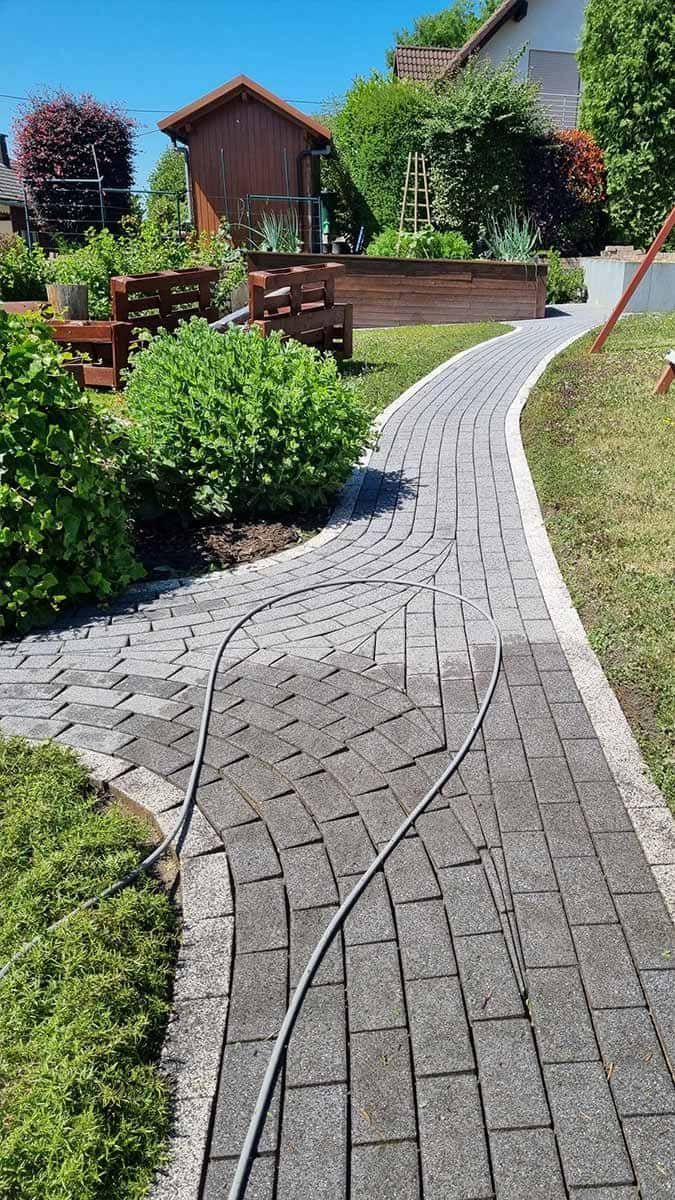 Ein gemauerter Gehweg in einem Garten, an dem ein Schlauch befestigt ist.
