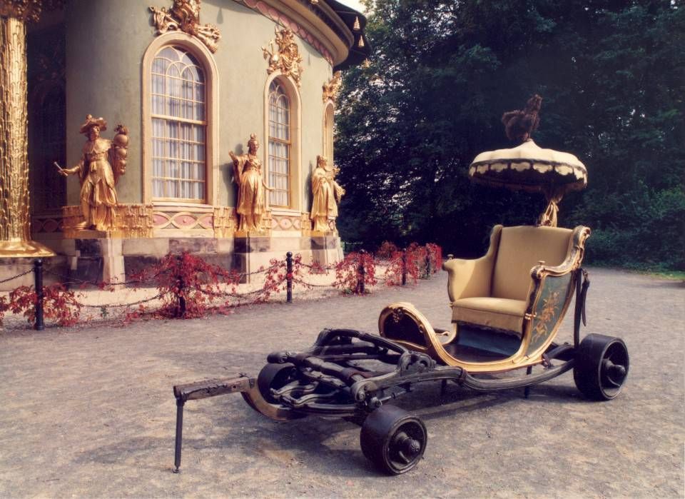 Verziertes gold- und beigefarbenes Oldtimer-Auto, geparkt vor einem historischen Gebäude mit Statuen und einem Brunnen