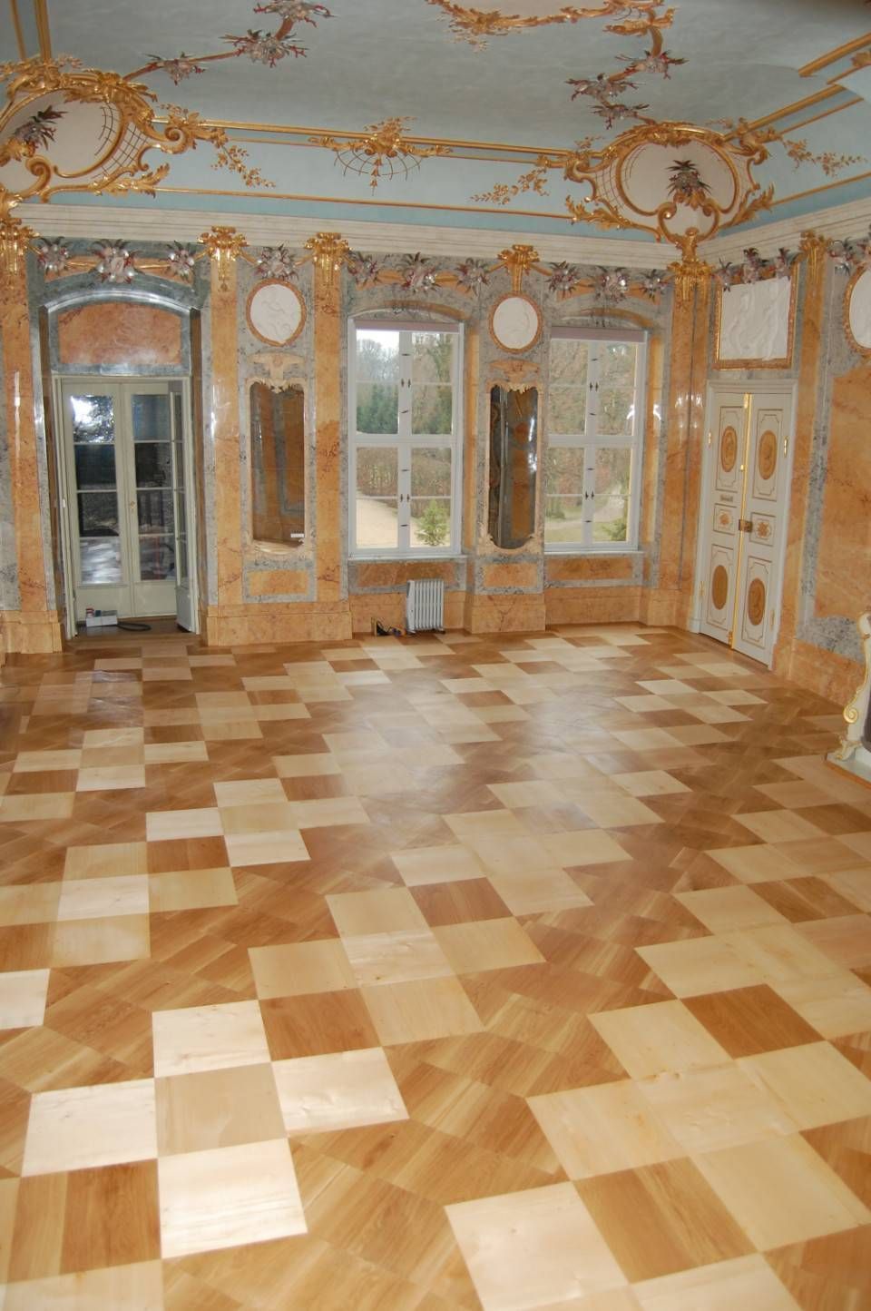 Prunkvoller leerer Ballsaal mit Parkettboden, goldenen Verzierungen, Spiegeln und hohen Fenstern