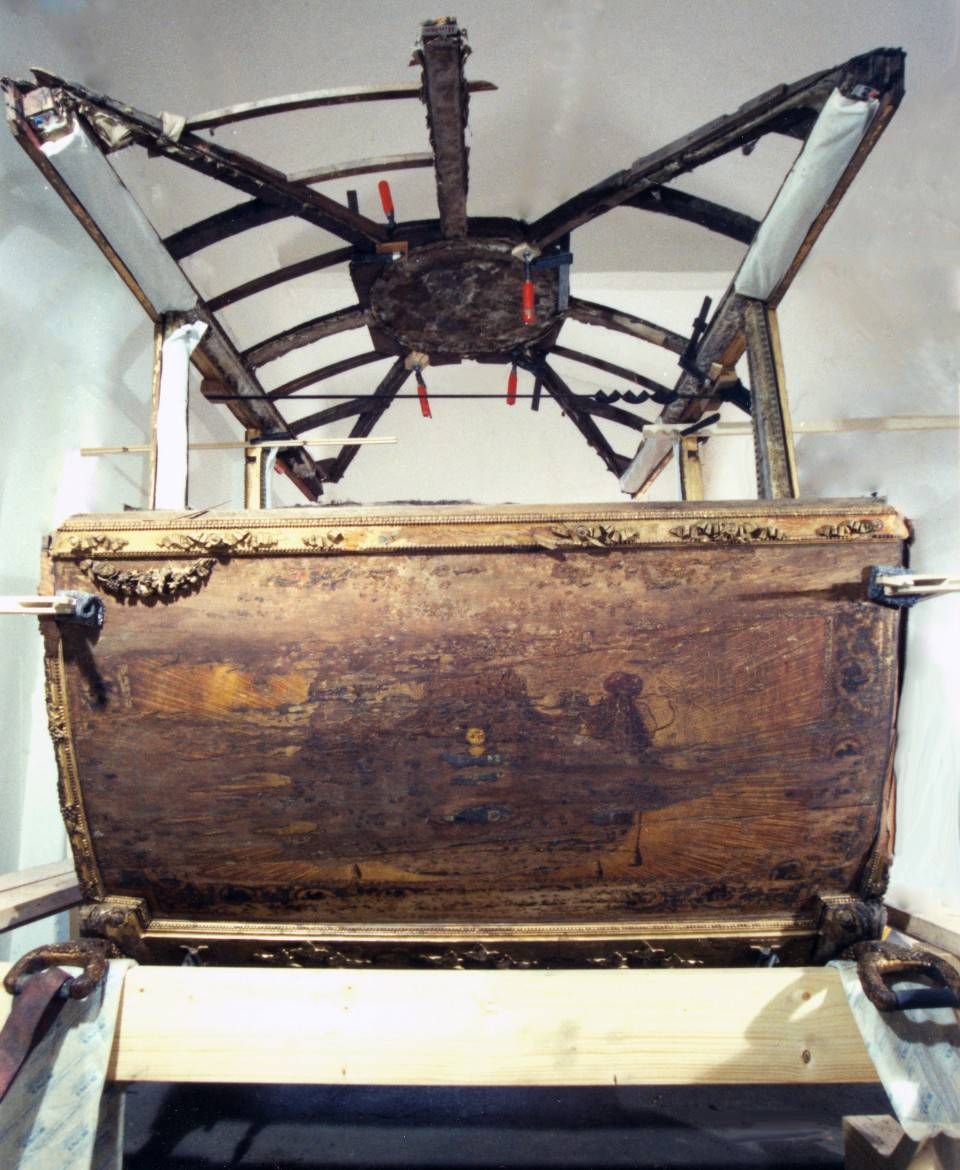 Eine alte Holztruhe mit einem darüber montierten, radähnlichen Metallgestell.