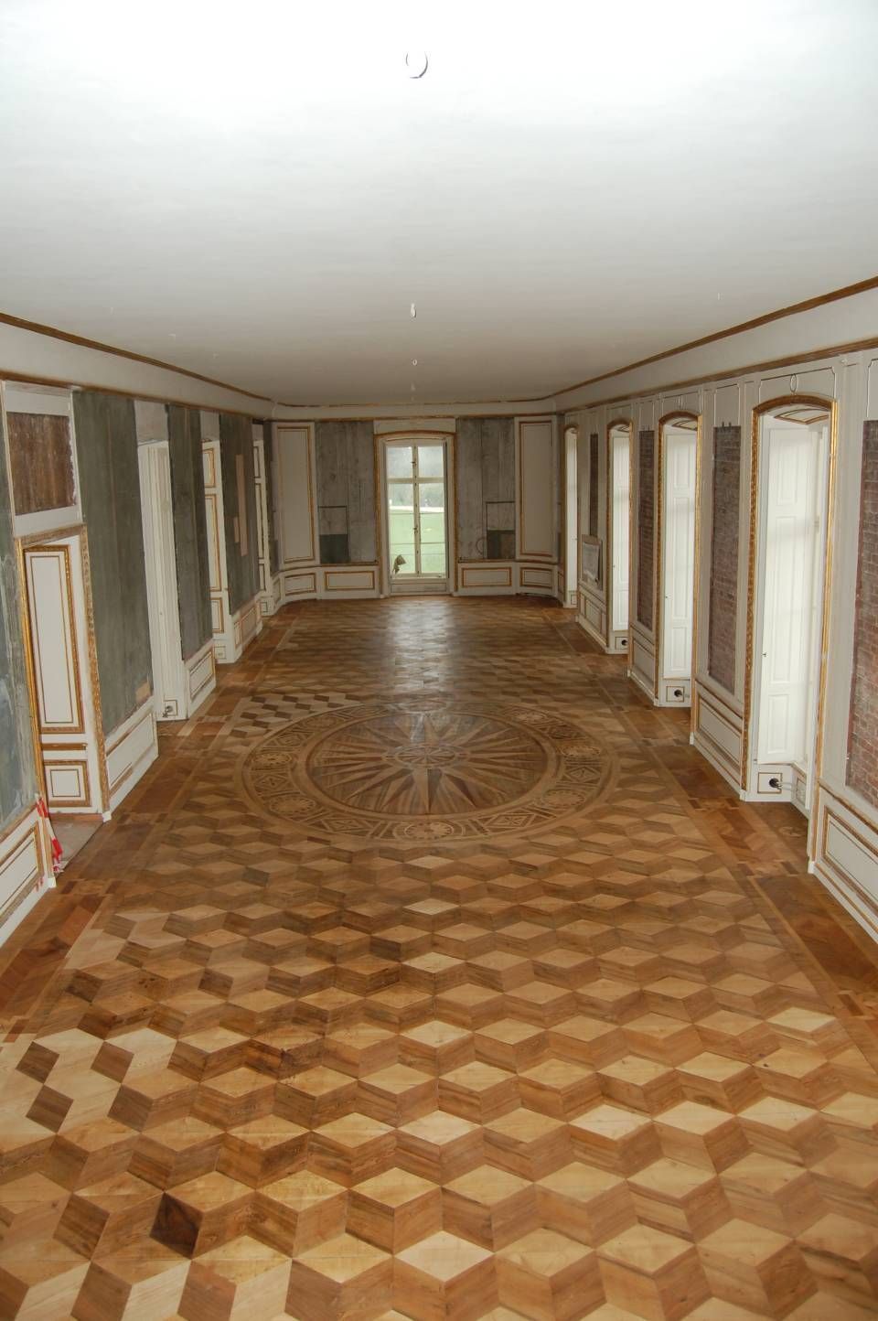 Leerer, kunstvoll gestalteter Flur mit gemustertem Holzboden und weißen Vertäfelungen, beleuchtet von Deckenleuchten