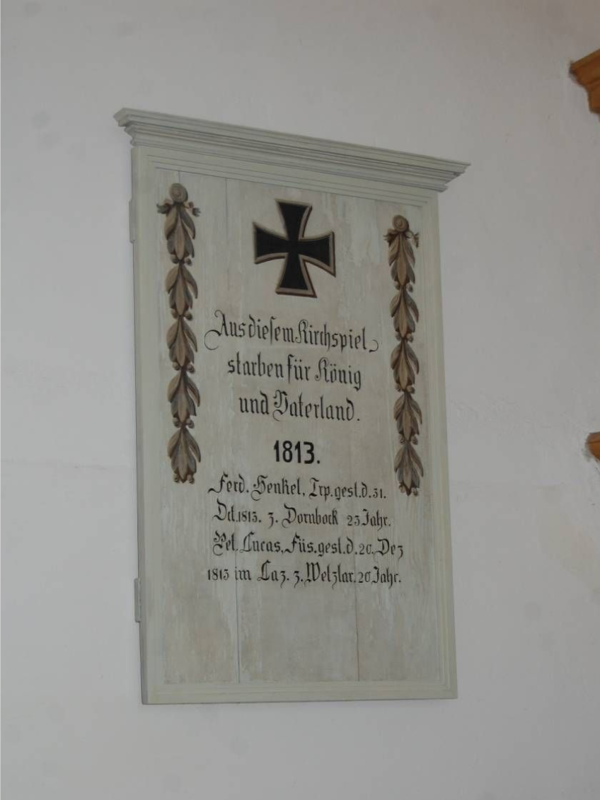 Steinerne Gedenktafel mit schwarzem Kreuz und Blumenornament, datiert auf 1813, an einer Wand angebracht.