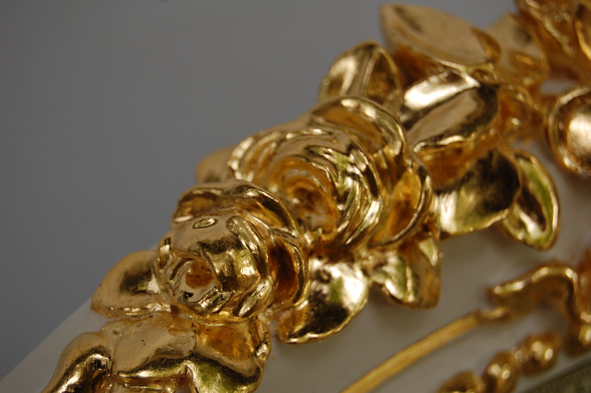 Nahaufnahme eines goldenen Kettenarmbands mit kunstvoll gearbeiteten Gliedern auf grauem Hintergrund