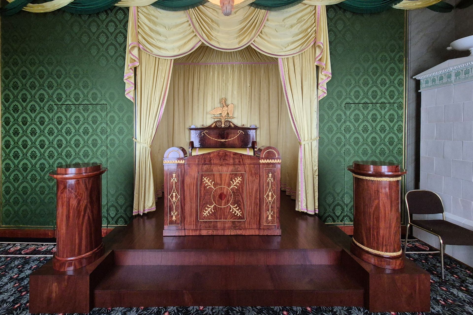 Verzierter Holzaltar mit goldenem Draperiebehang in einem Raum mit grünen Wänden, flankiert von passenden Sockeln.