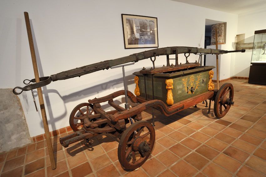 Antiker hölzerner Bauernwagen mit großen Rädern, der auf einem Fliesenboden in einem Innenraum ausgestellt ist.