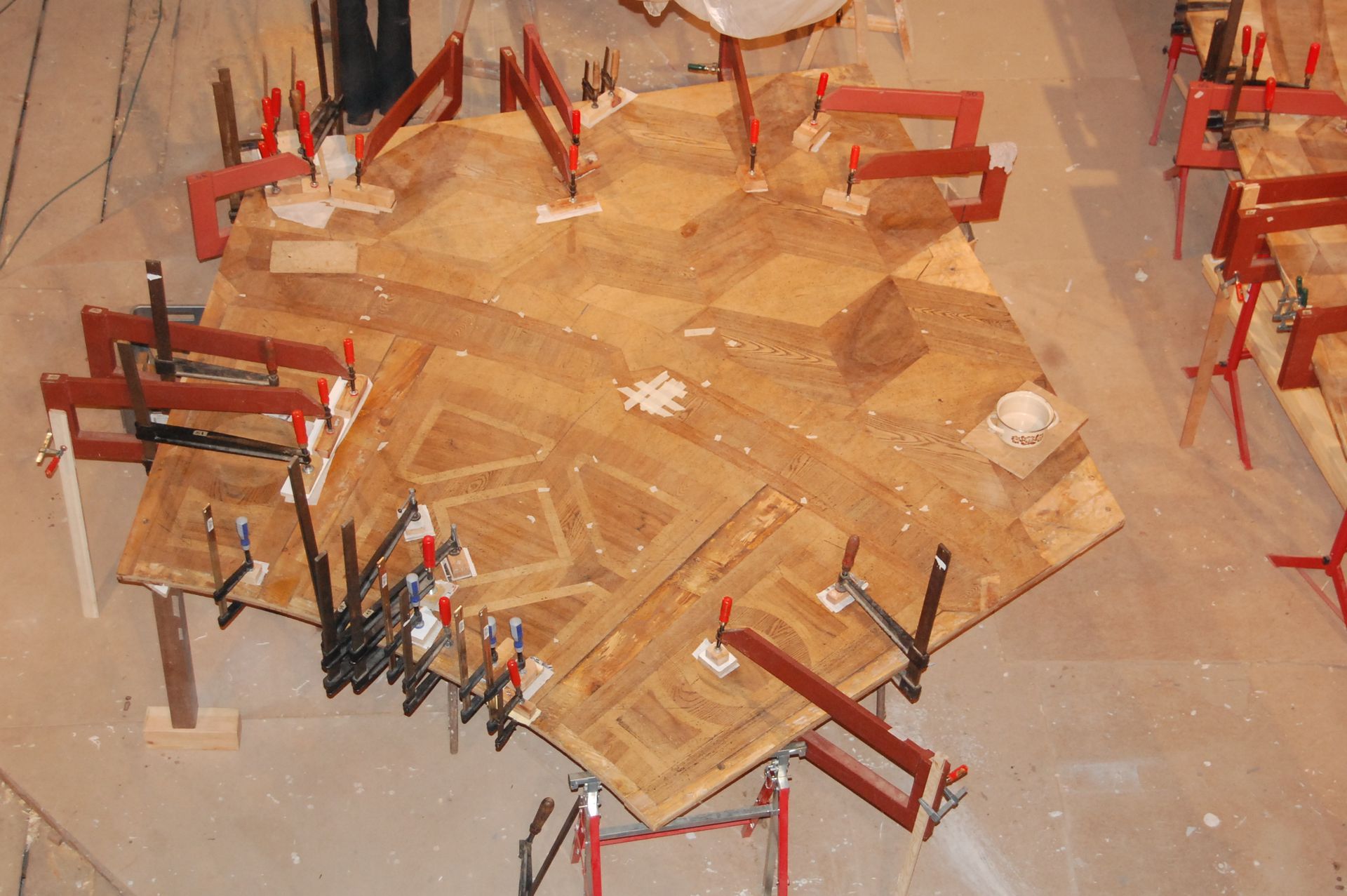 Eine Holzbrettkonstruktion, die von roten Metallklemmen auf dem Boden gehalten wird.