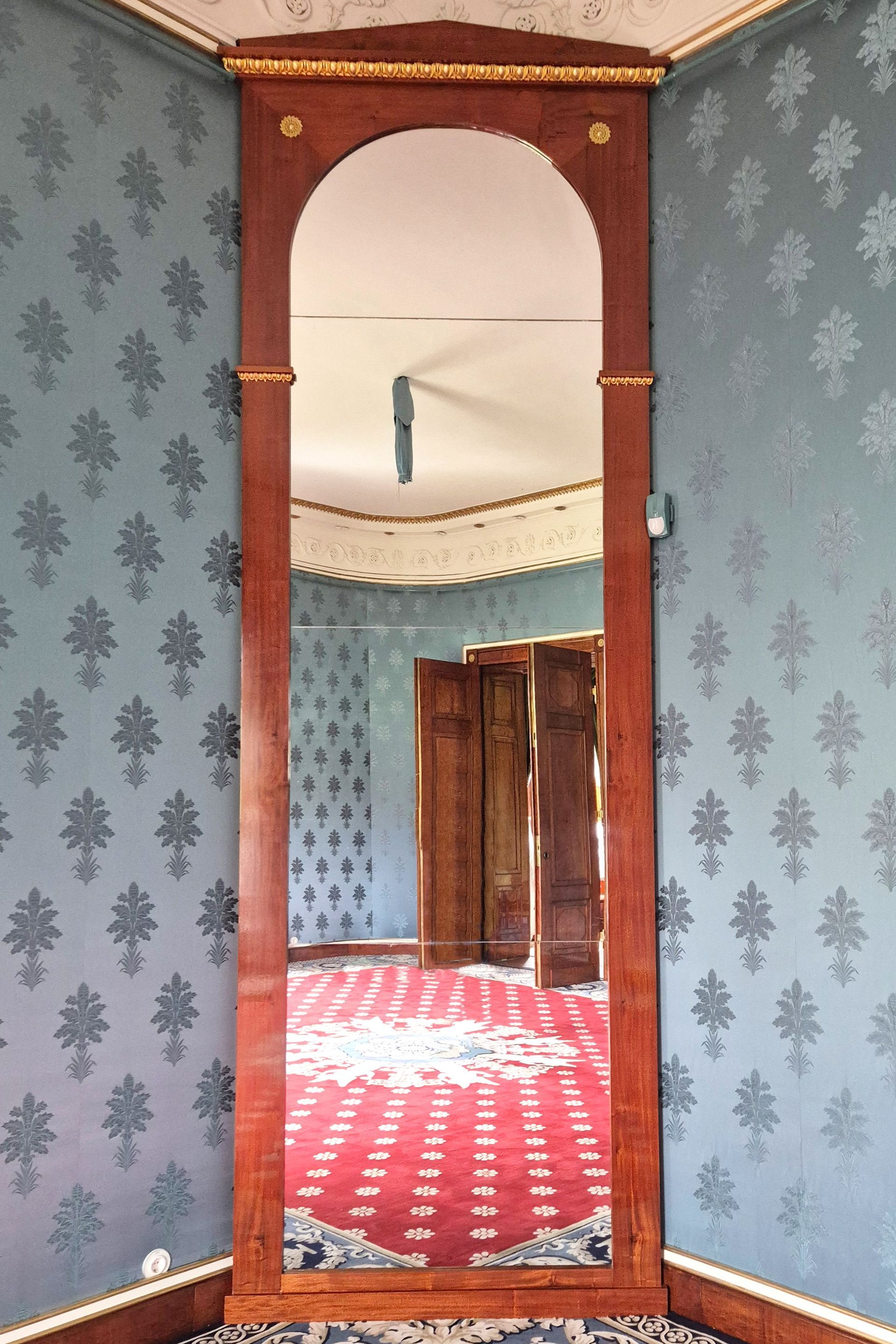 Ein Rundbogen in einem blau gemusterten Raum mit Blick auf einen rot ausgelegten Flur mit Holztüren.