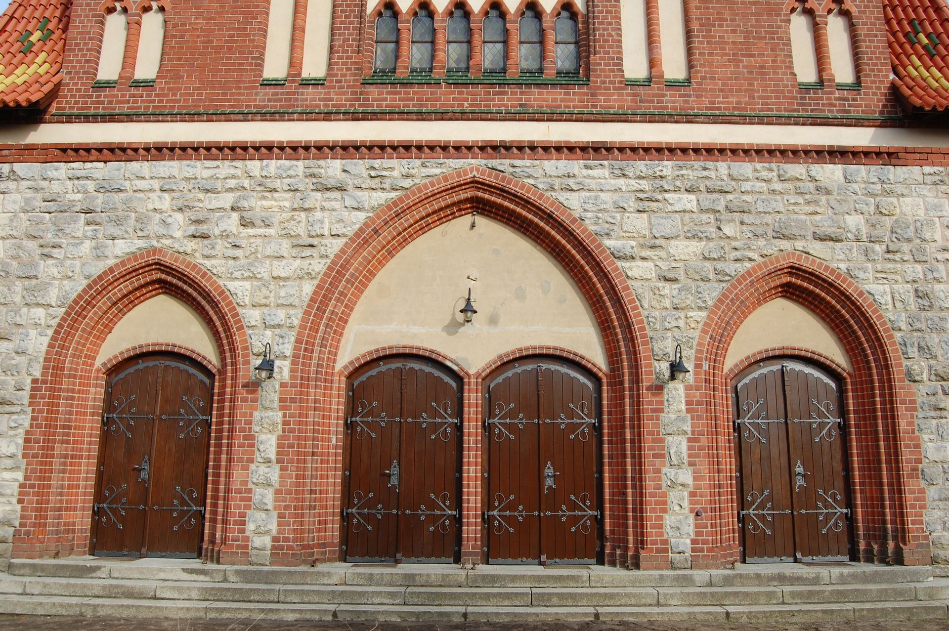Backsteinfassade einer Kirche mit drei gewölbten Holztüren und Steinmauern