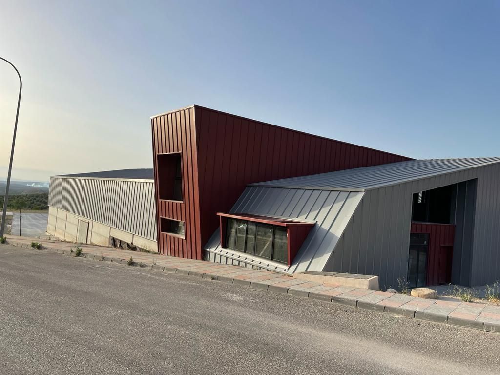 Un gran edificio con un techo rojo y gris se encuentra al costado de una carretera.